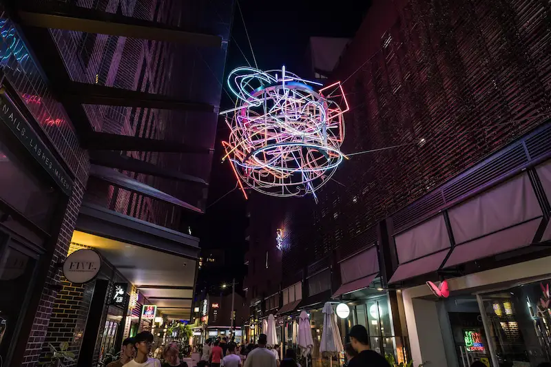 A neon art installation in Sydney Chinatown at night, with people walking in the background
